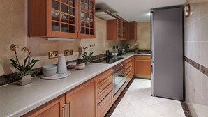 A kitchen with wooden cabinets, a stainless steel refrigerator, and a marble countertop. - Hyatt Regency London The Churchill (London)