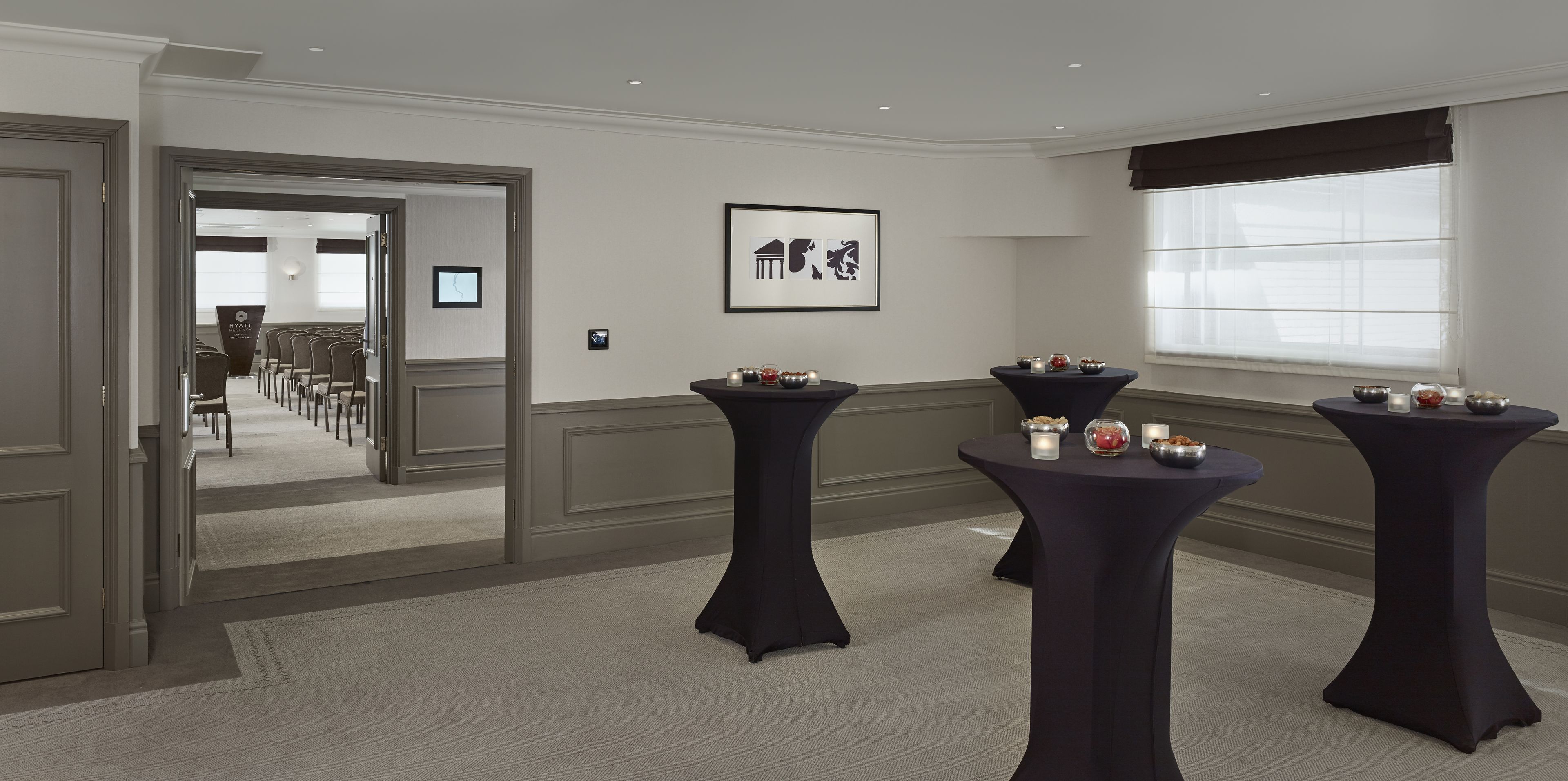 Un salón de conferencias con una larga mesa y sillas, un cuadro en la pared y una ventana con persianas.