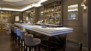 A bar area with a long counter, bar stools, and a well-stocked liquor shelf. - Hyatt Regency London The Churchill (London)