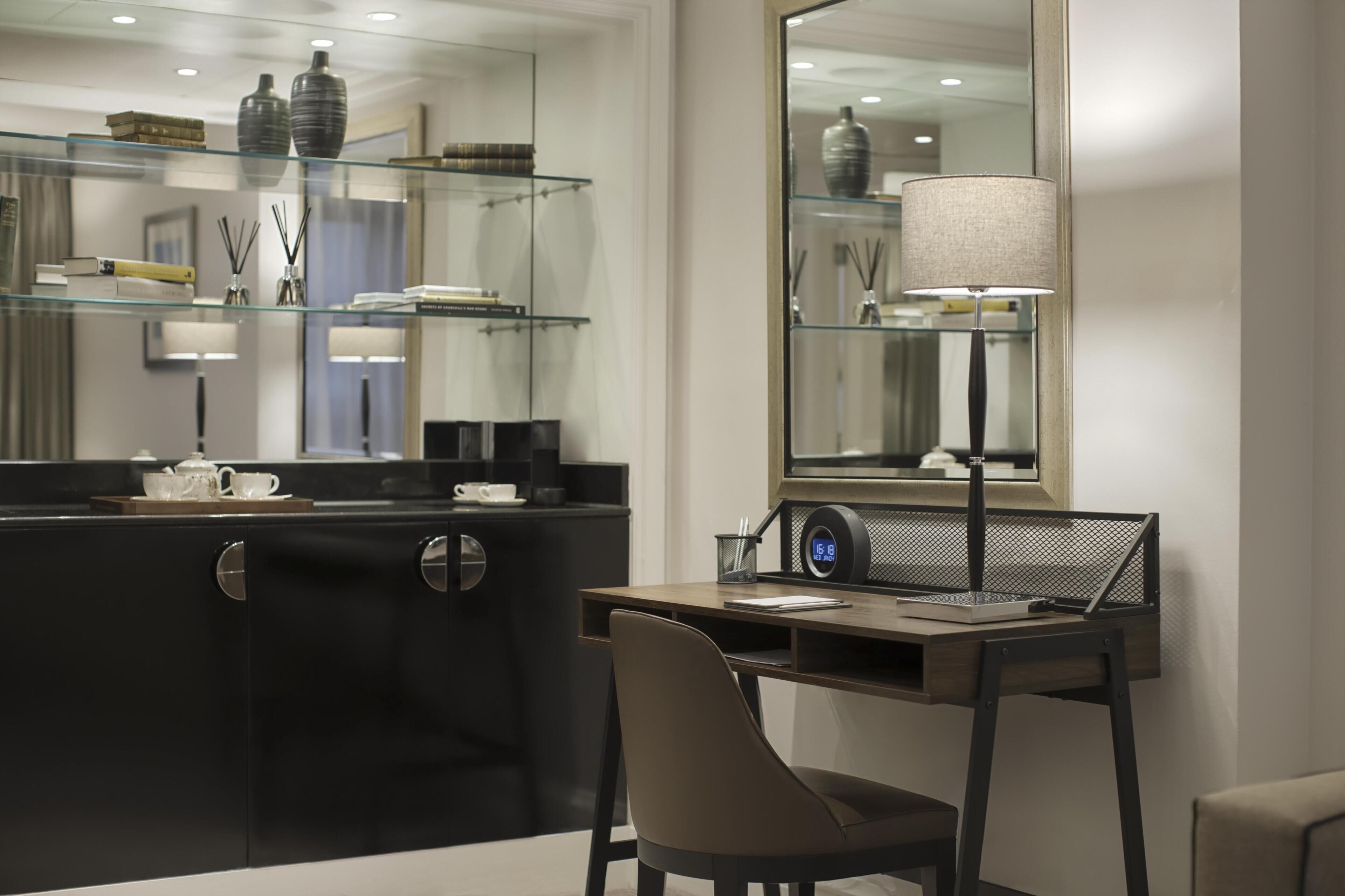 A modern hotel room with a desk, chair, and a large mirror.