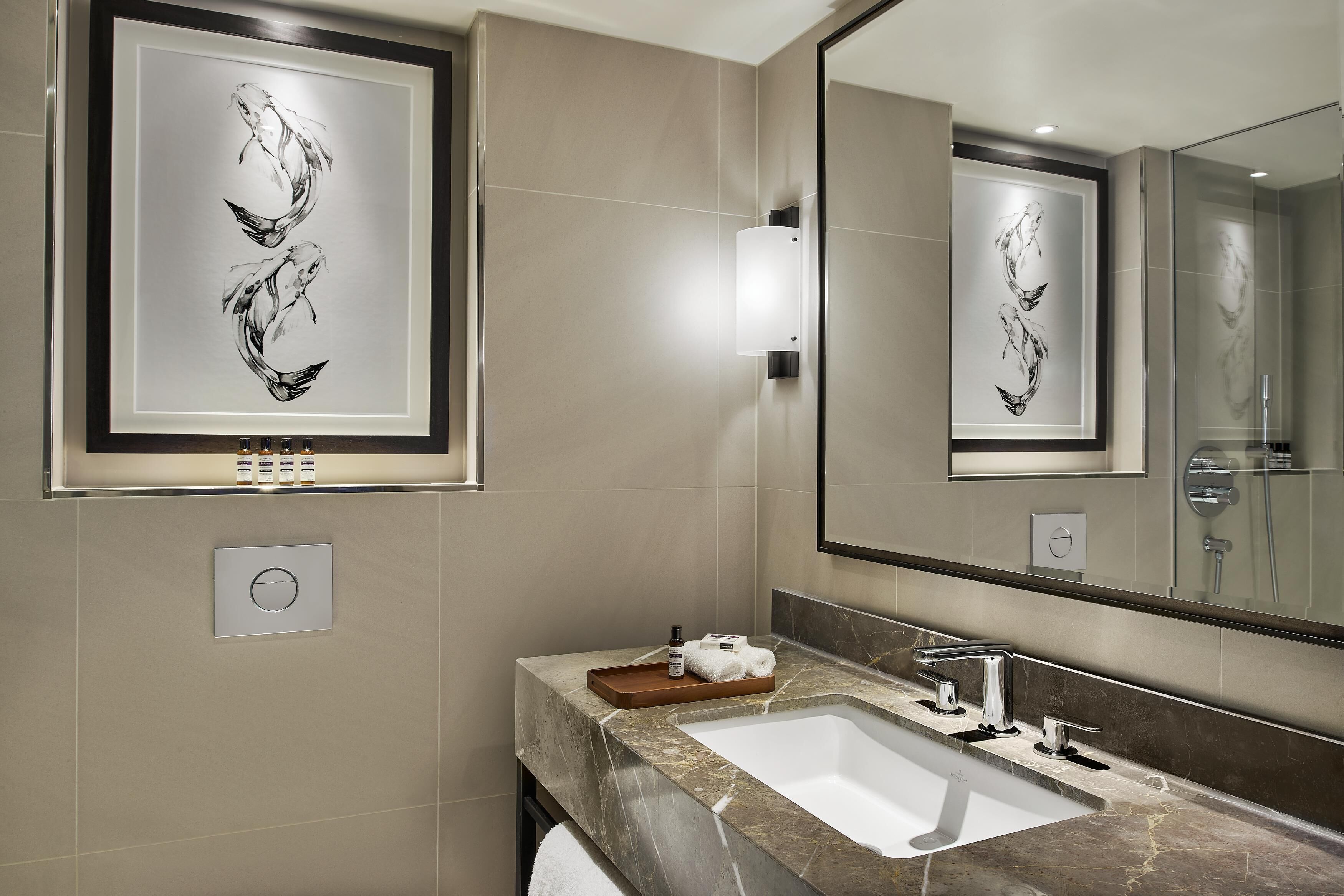 A modern bathroom with a large mirror, framed artwork, a marble sink, and a towel rack.