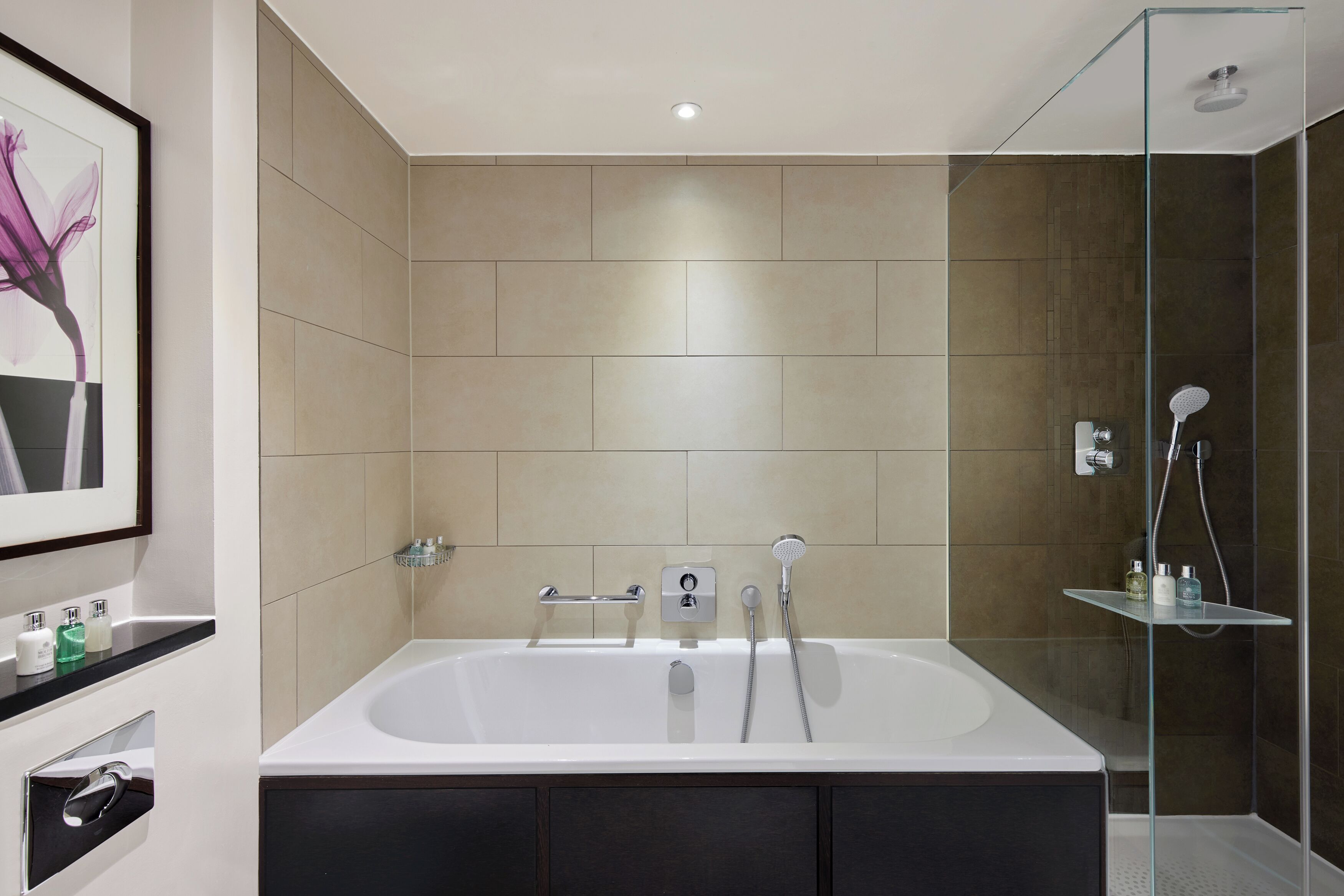 A modern bathroom with a large bathtub, a glass shower enclosure, and a framed artwork on the wall.