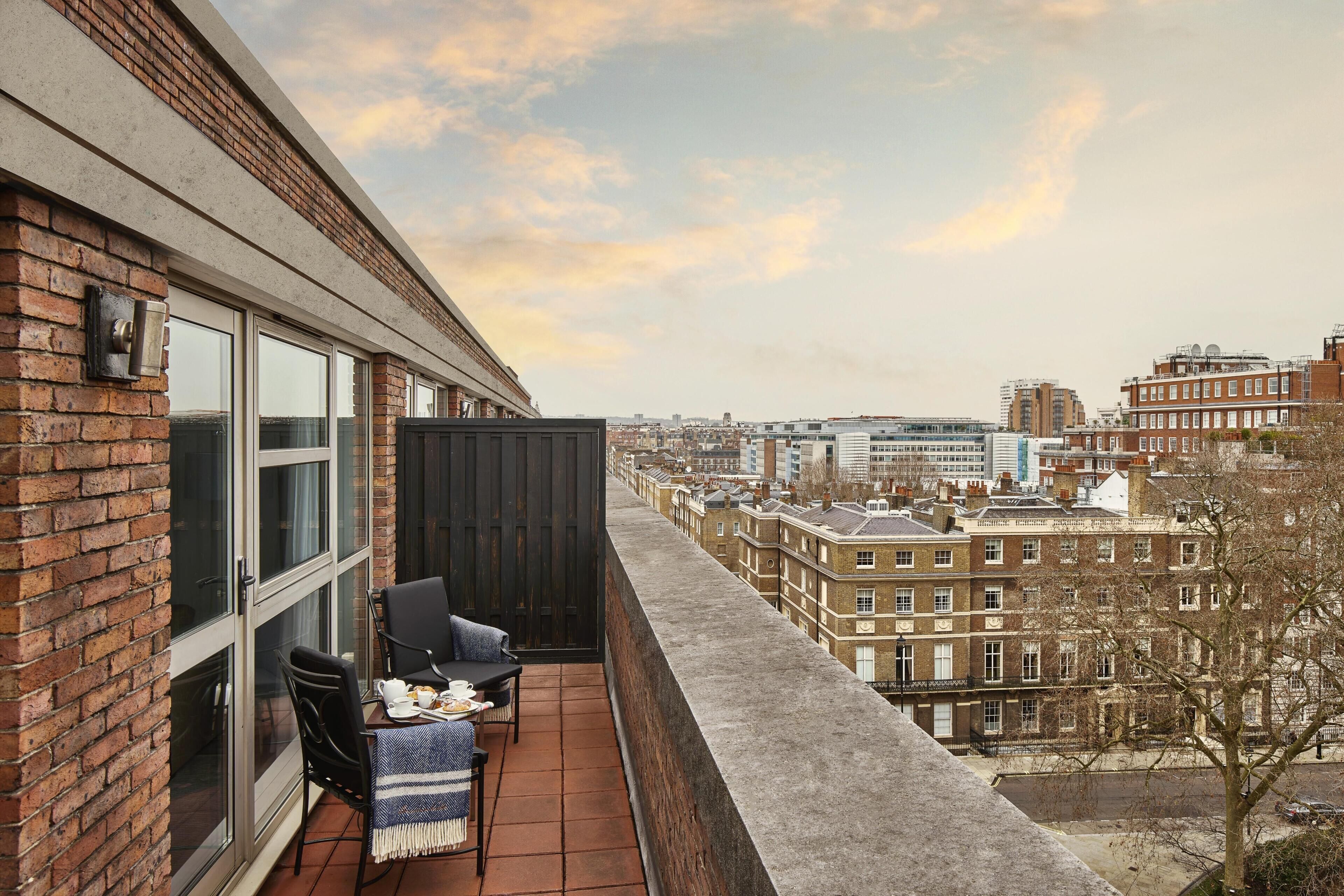 A balcony with a view of the cityscape, featuring brick buildings and a clear sky.