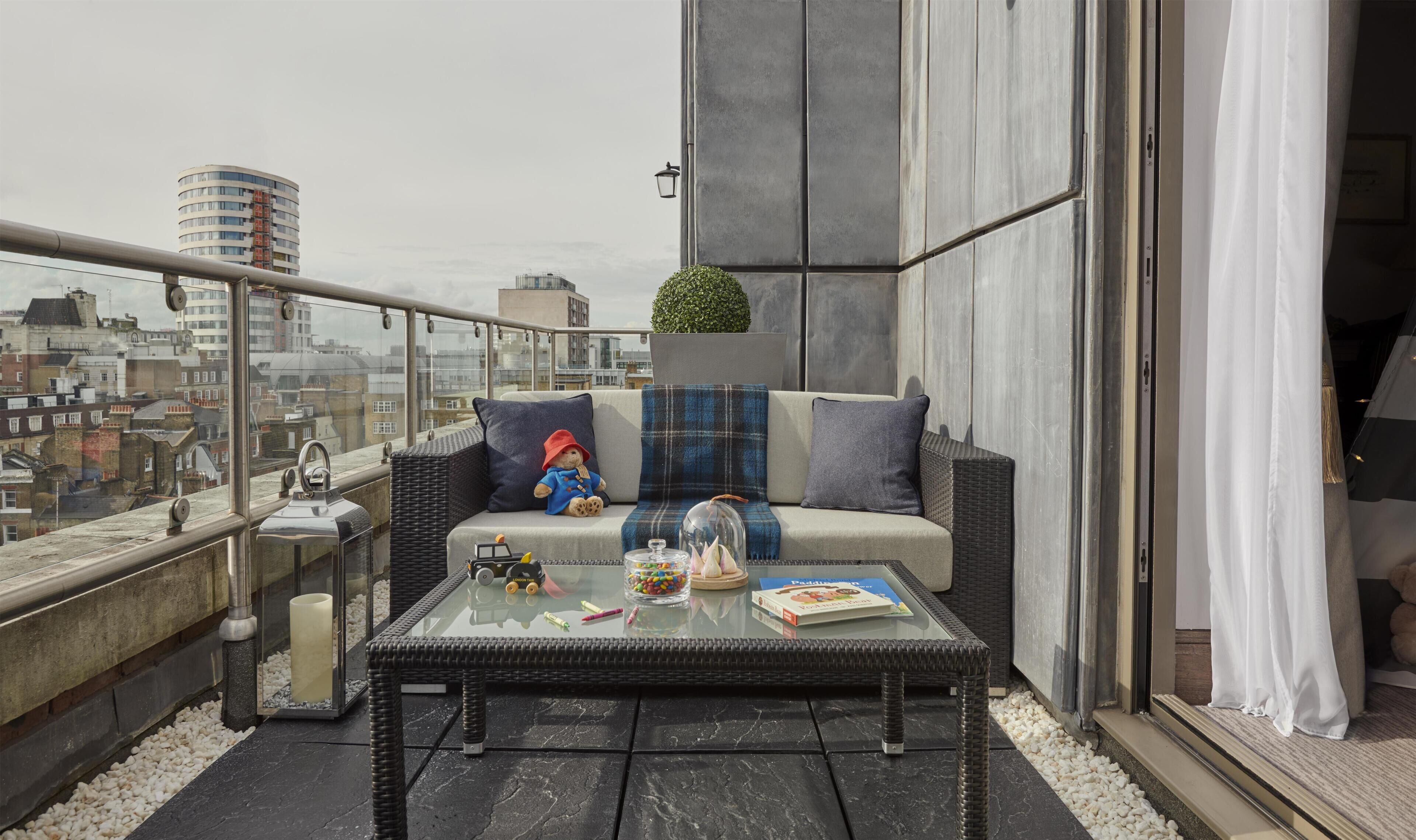 A balcony with a wicker sofa, a glass coffee table, and a view of the cityscape.
