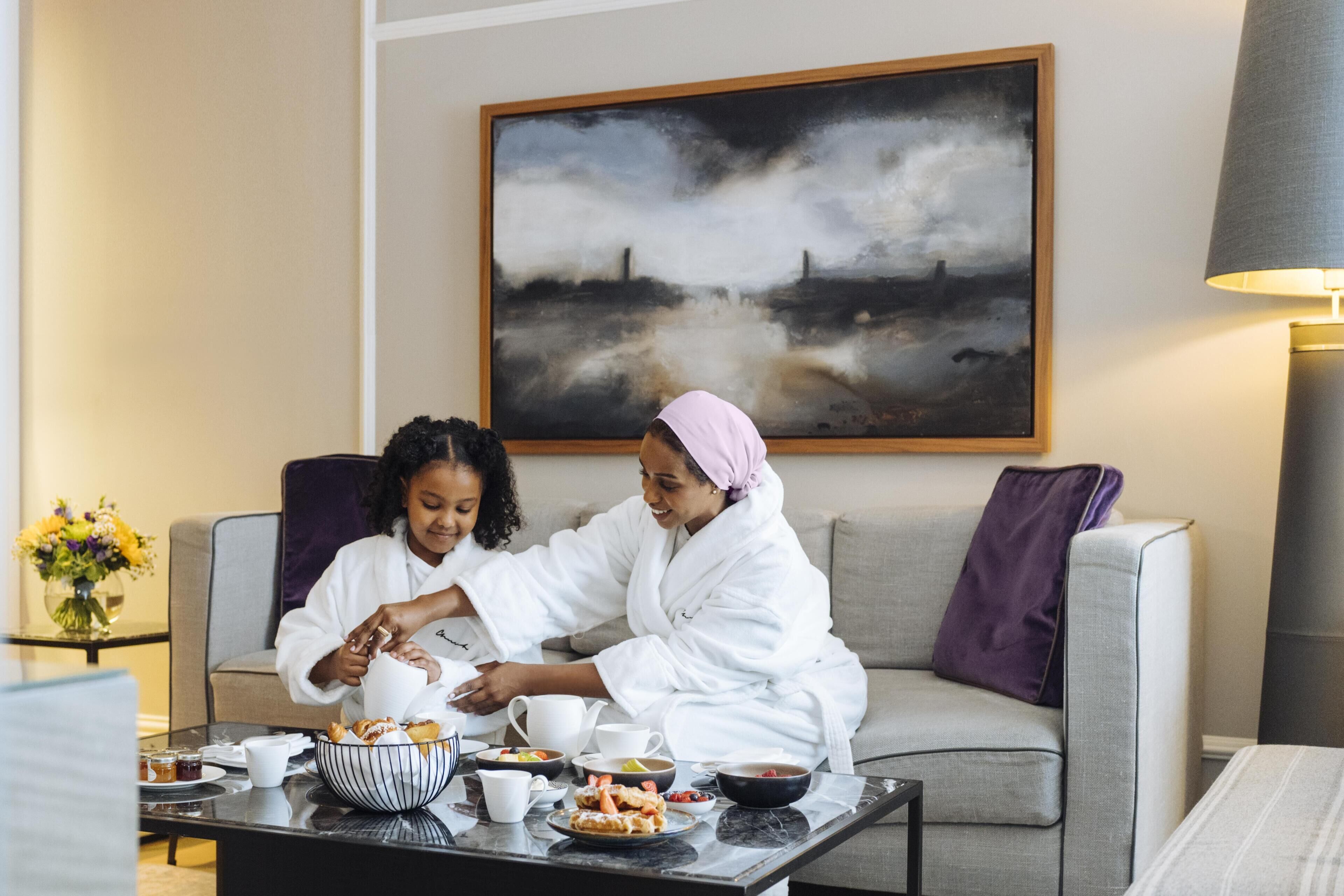 A room with a sofa, a coffee table with breakfast items, and a painting on the wall.