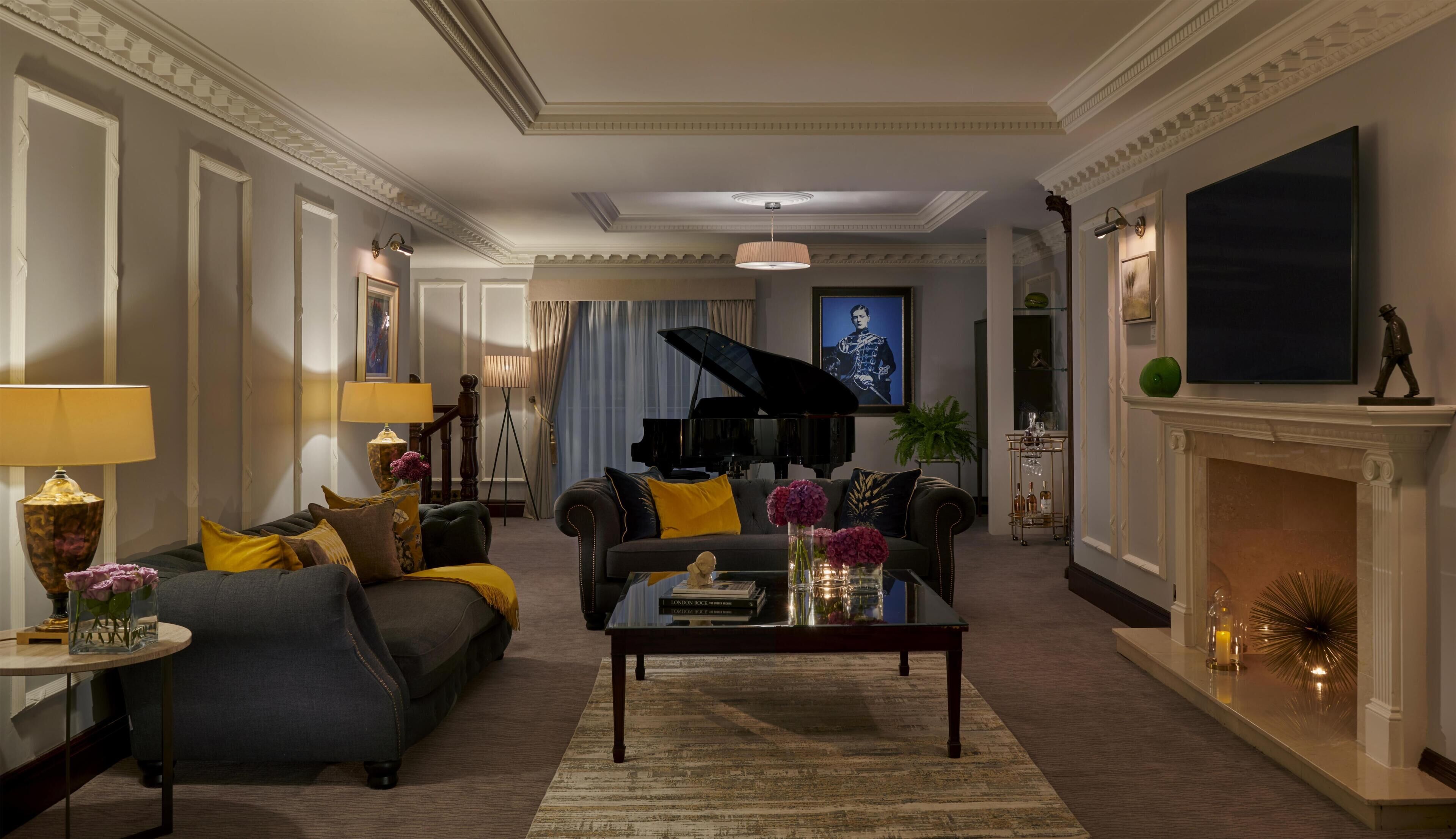 Un salon comprenant un piano à queue, un ensemble de canapés, une table basse agrémentée d’objets décoratifs et une cheminée.