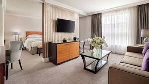 A hotel room with a bed, a TV, a glass coffee table, a sofa, a desk, and a chair. - Hyatt Regency London The Churchill (London)