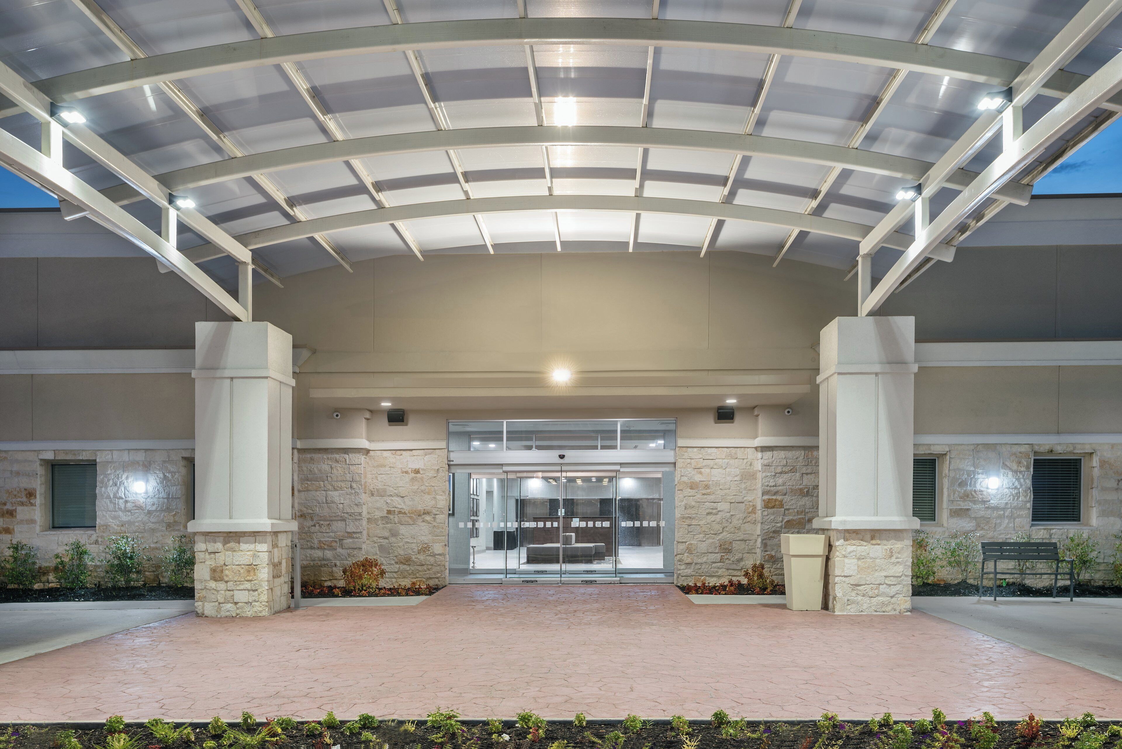 A covered entrance with a glass door, stone pillars, and a paved walkway.