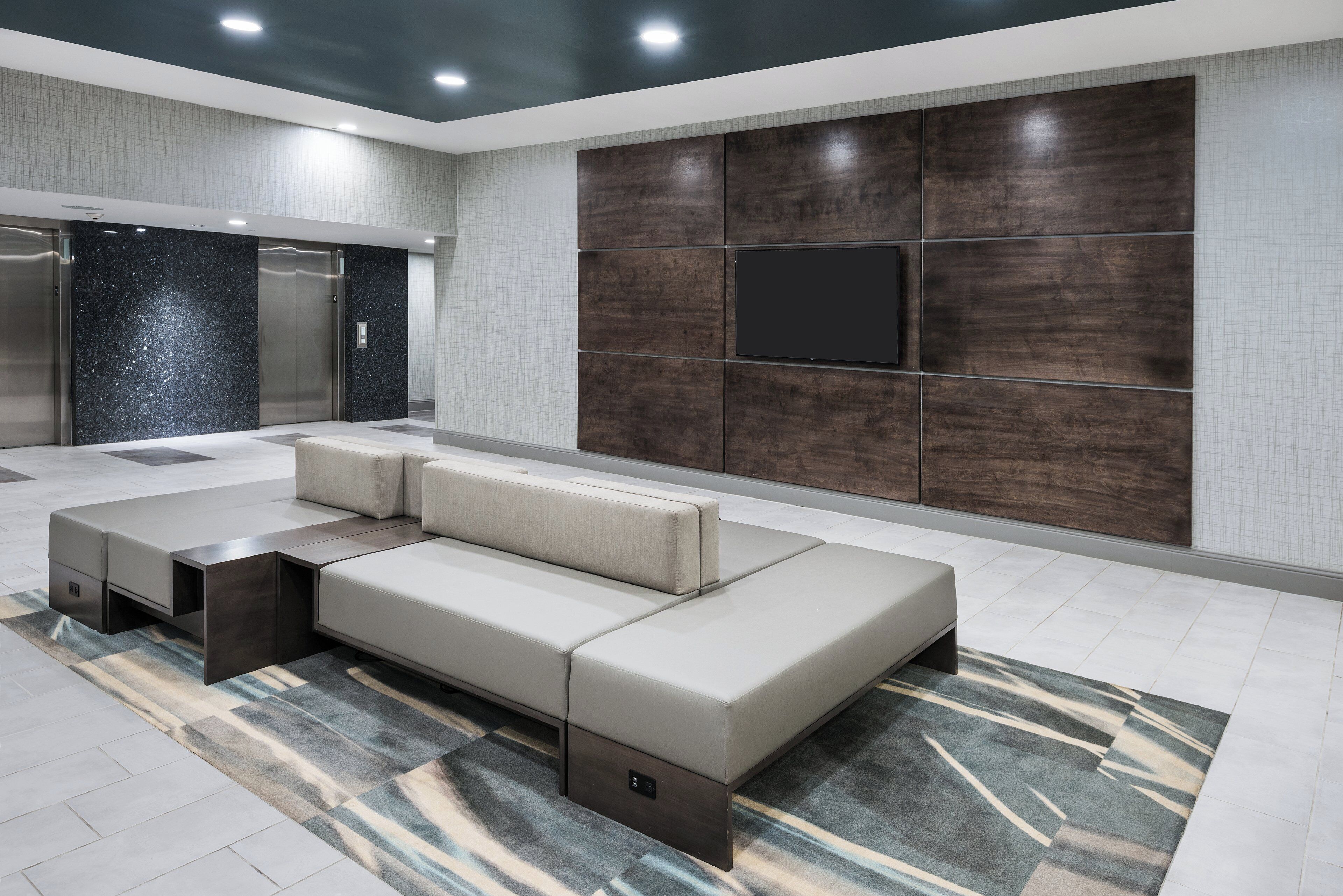 A modern lobby with a sectional sofa, a flat-screen TV, and a patterned rug.