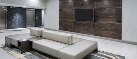 A modern lobby with a sectional sofa, a flat-screen TV, and a patterned rug.