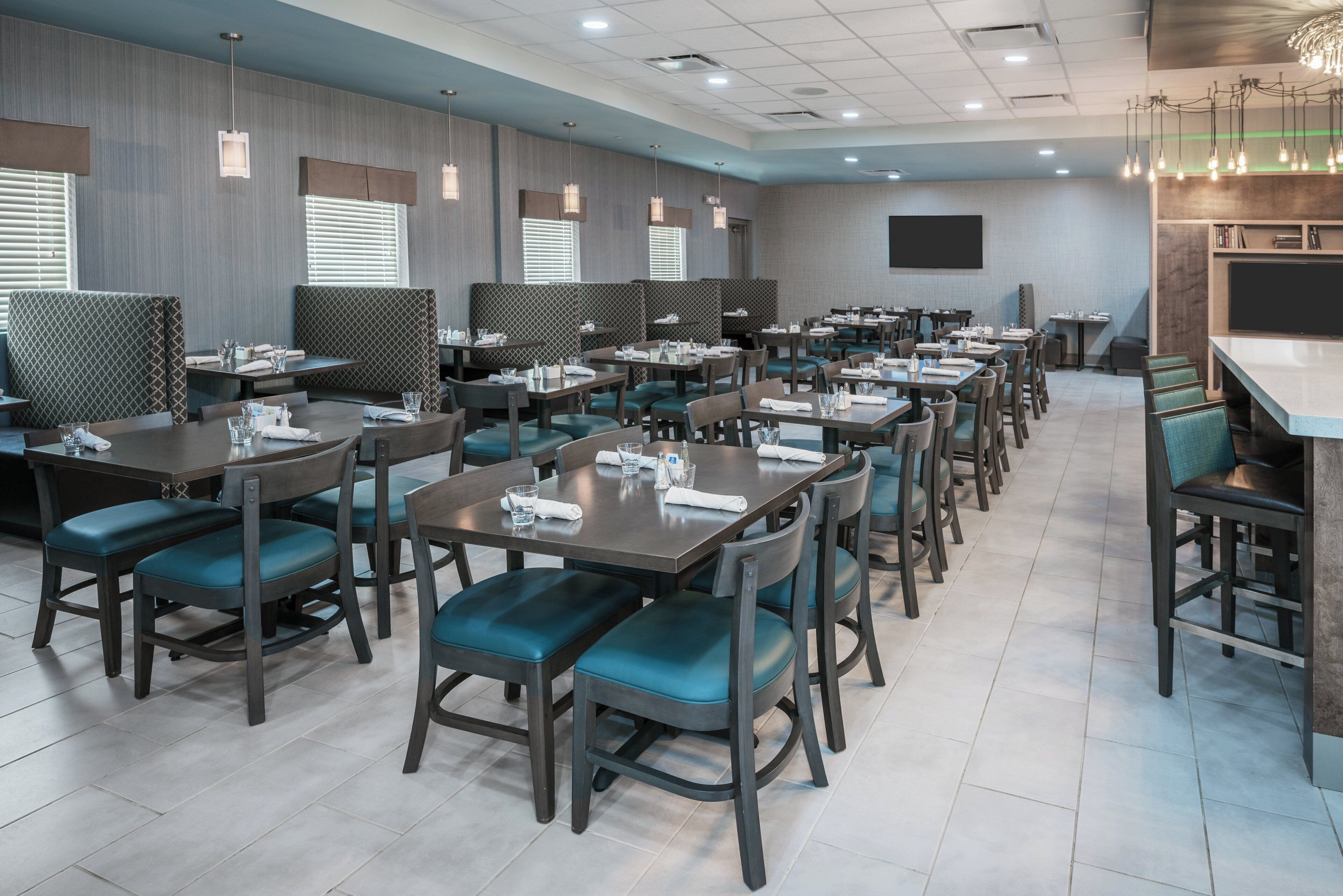 A hotel dining area with multiple tables and chairs, some with privacy partitions.