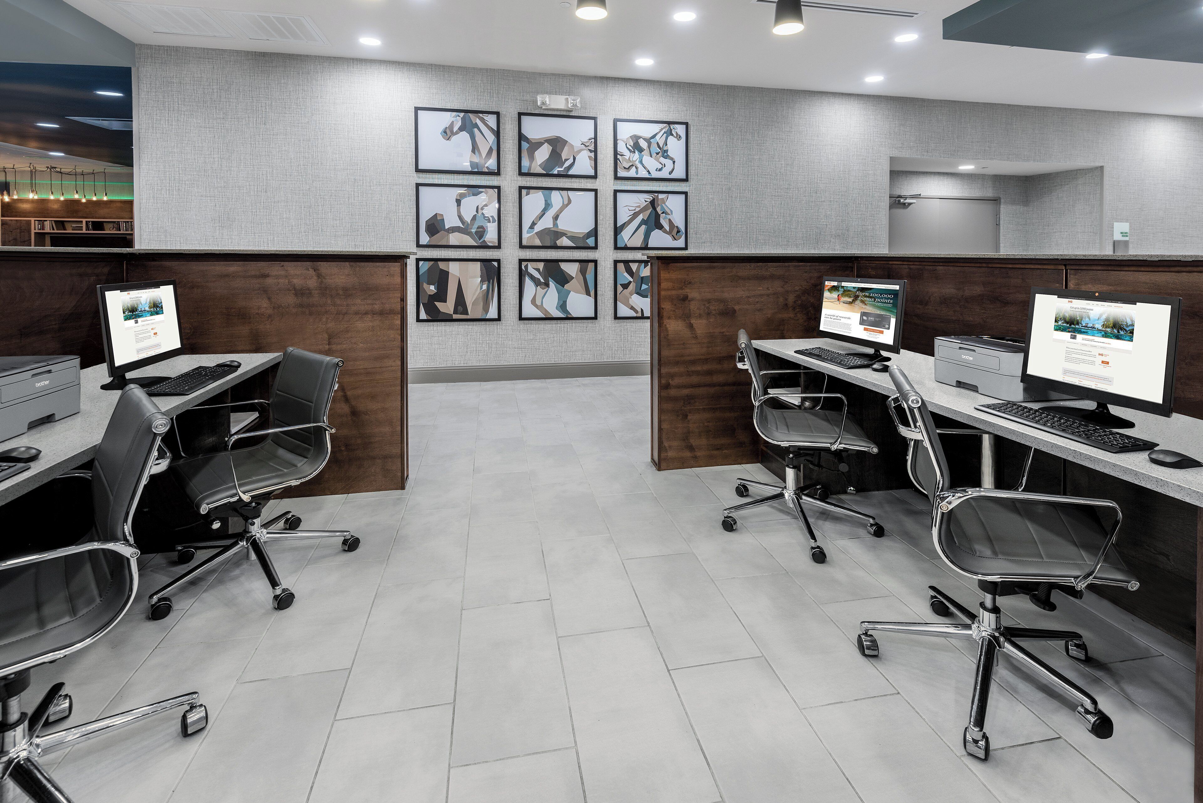 A modern office space with two desks, each with a computer, ergonomic chairs, and framed artwork on the wall.