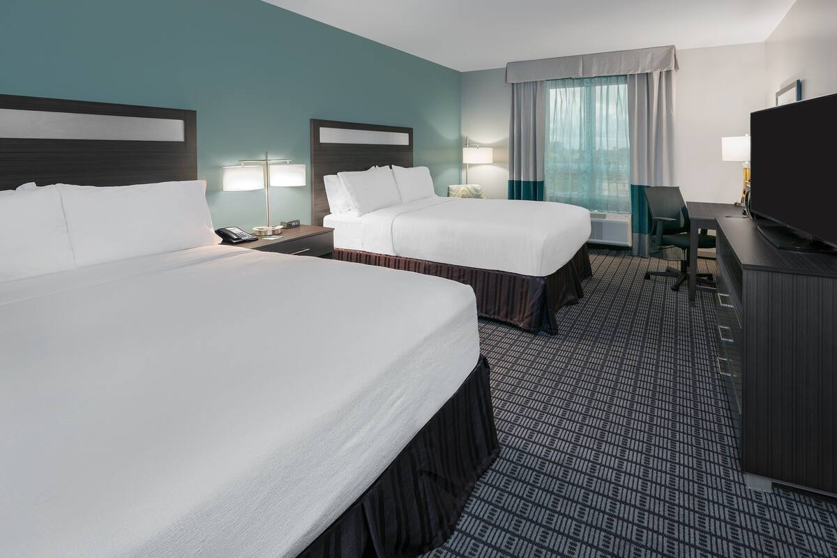 Ett hotellrum med två sängar, ett skrivbord, en tv och ett fönster med gardiner.