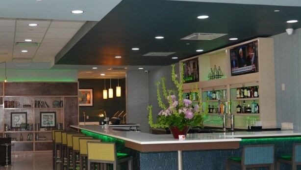 A modern bar area with a counter, seating, and a television screen. - Holiday Inn Beaumont East - Medical Ctr Area by IHG (Beaumont)