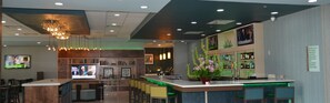 A modern bar area with a counter, seating, and a television screen. - Holiday Inn Beaumont East - Medical Ctr Area by IHG (Beaumont)