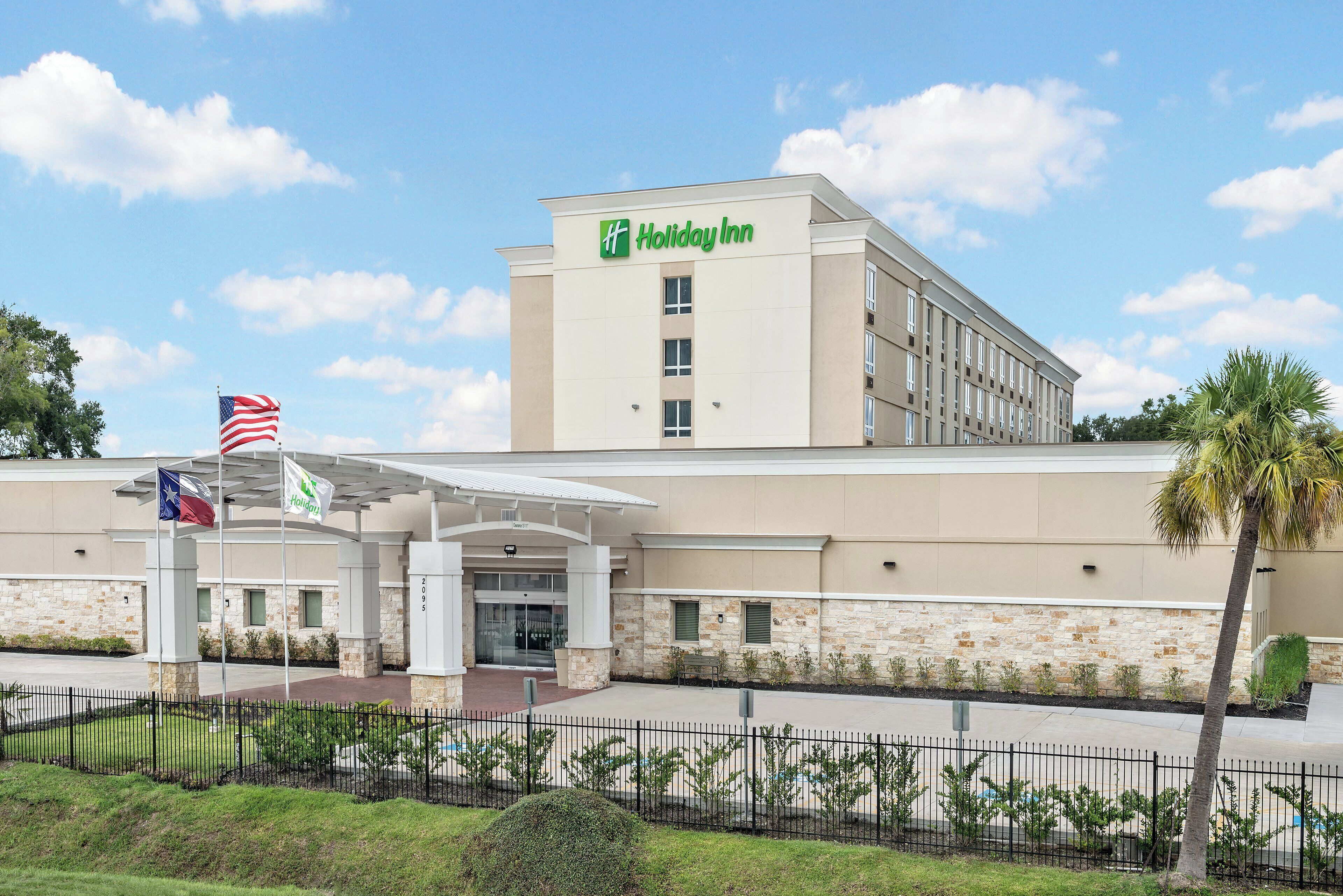 A Holiday Inn hotel with a modern facade, a covered entrance, and a flagpole with the Texas state flag.