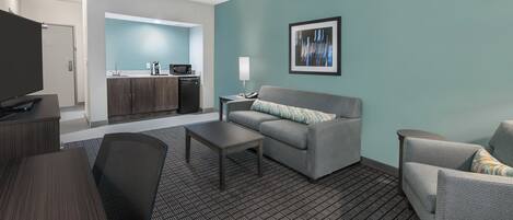 Una habitación de hotel moderna con kitchenette, un sofá, una mesa de centro y un televisor.