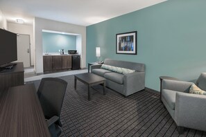 A modern hotel room with a kitchenette, a sofa, a coffee table, and a TV. - Holiday Inn Beaumont East - Medical Ctr Area by IHG (Beaumont)