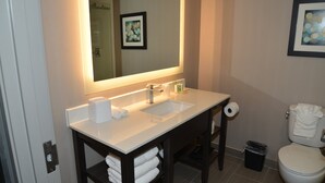 A bathroom with a white sink, mirror, and toilet. There are towels and a trash can visible. - Holiday Inn Beaumont East - Medical Ctr Area by IHG (Beaumont)
