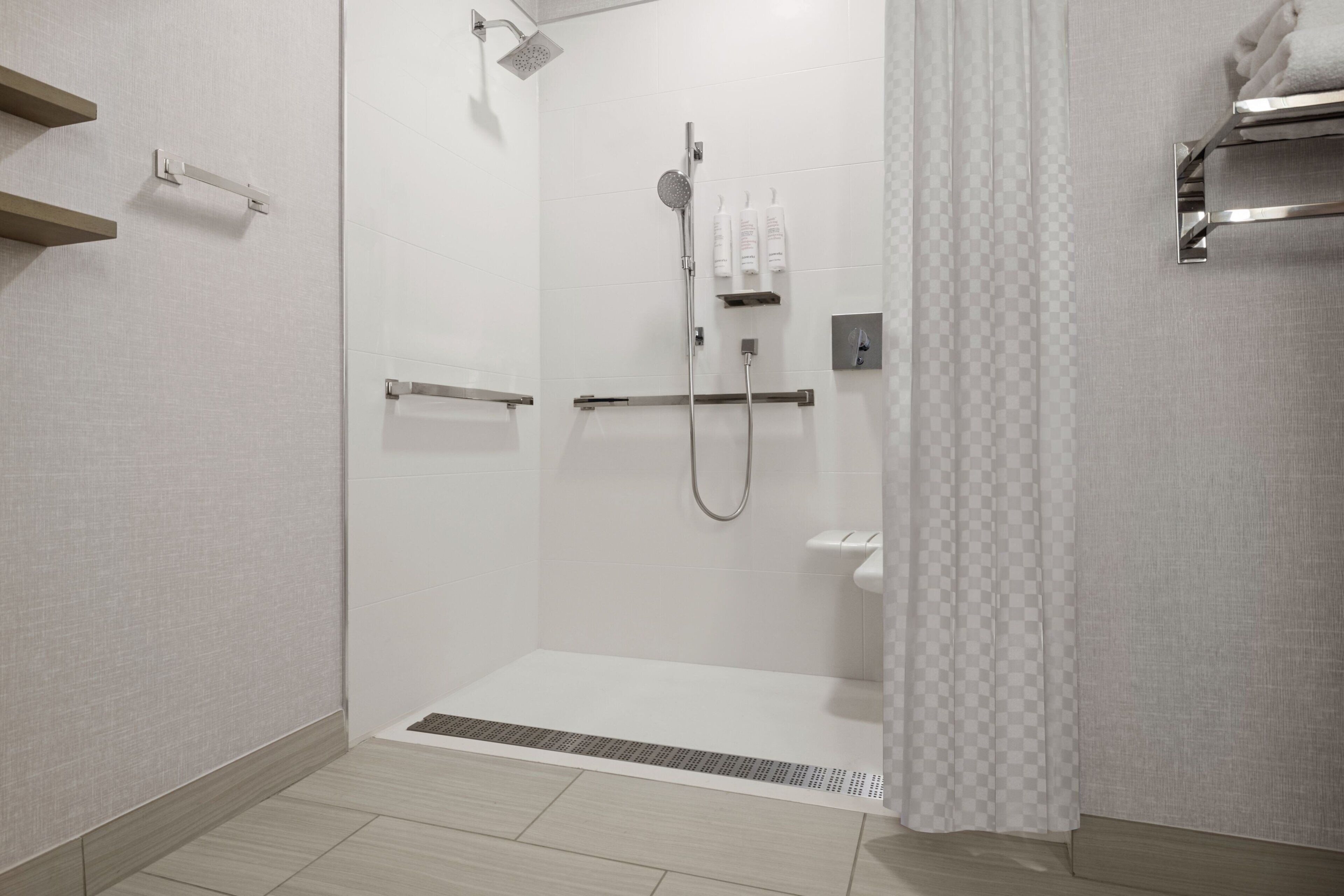 A modern shower area with a handheld showerhead, a wall-mounted faucet, and a handheld showerhead. There are two towel racks on the wall, and a shower curtain is partially drawn.