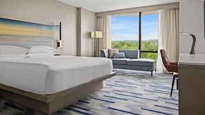 A hotel room with a large bed, a sofa, a desk, and a view of the outdoors.