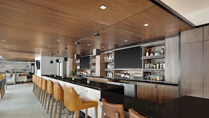 Un área de bar moderna con una barra alargada, sillas de madera y estantes llenos de botellas.