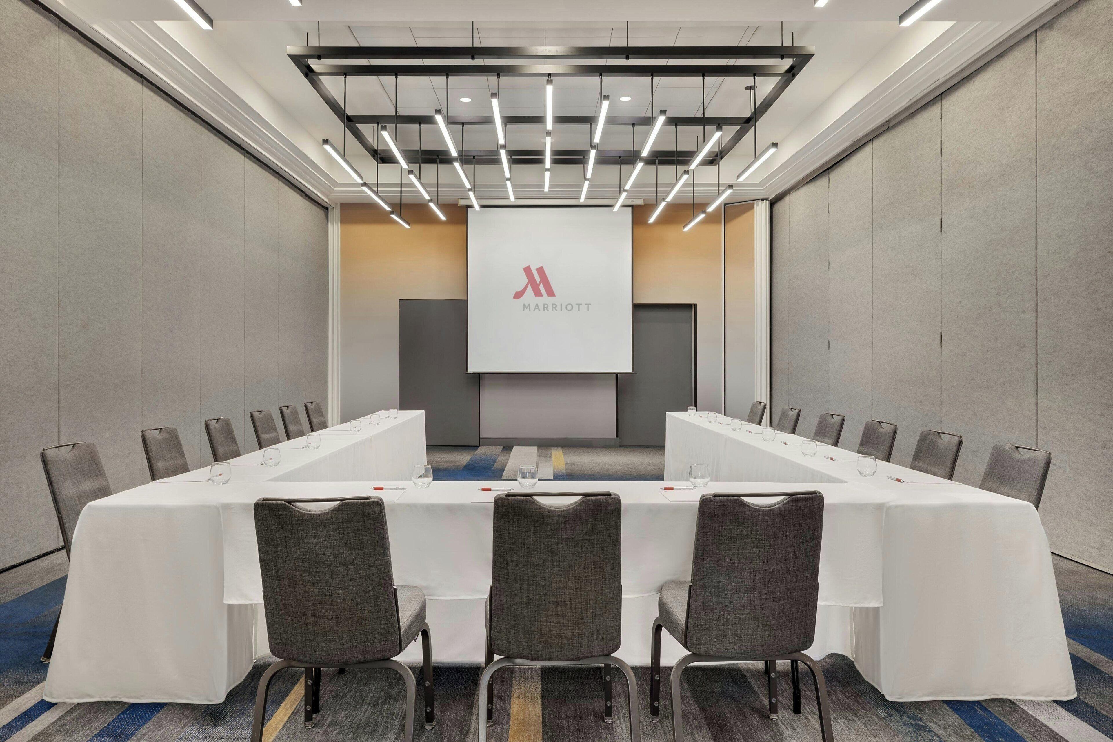 Ein Konferenzraum mit einem langen Tisch, Stühlen und einem großen Bildschirm, der das Marriott-Logo zeigt.