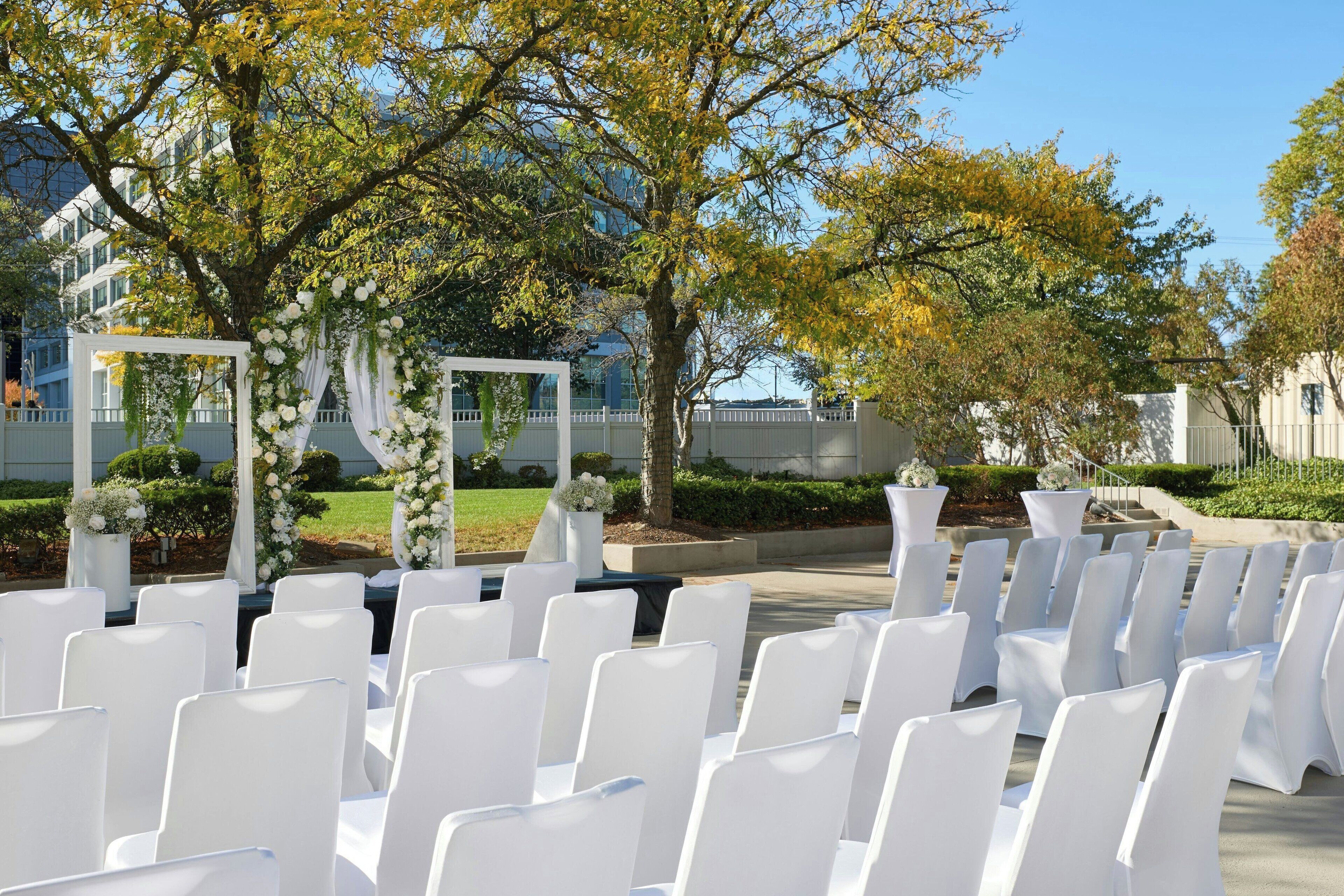 An outdoor wedding setup with white chairs and floral decorations.