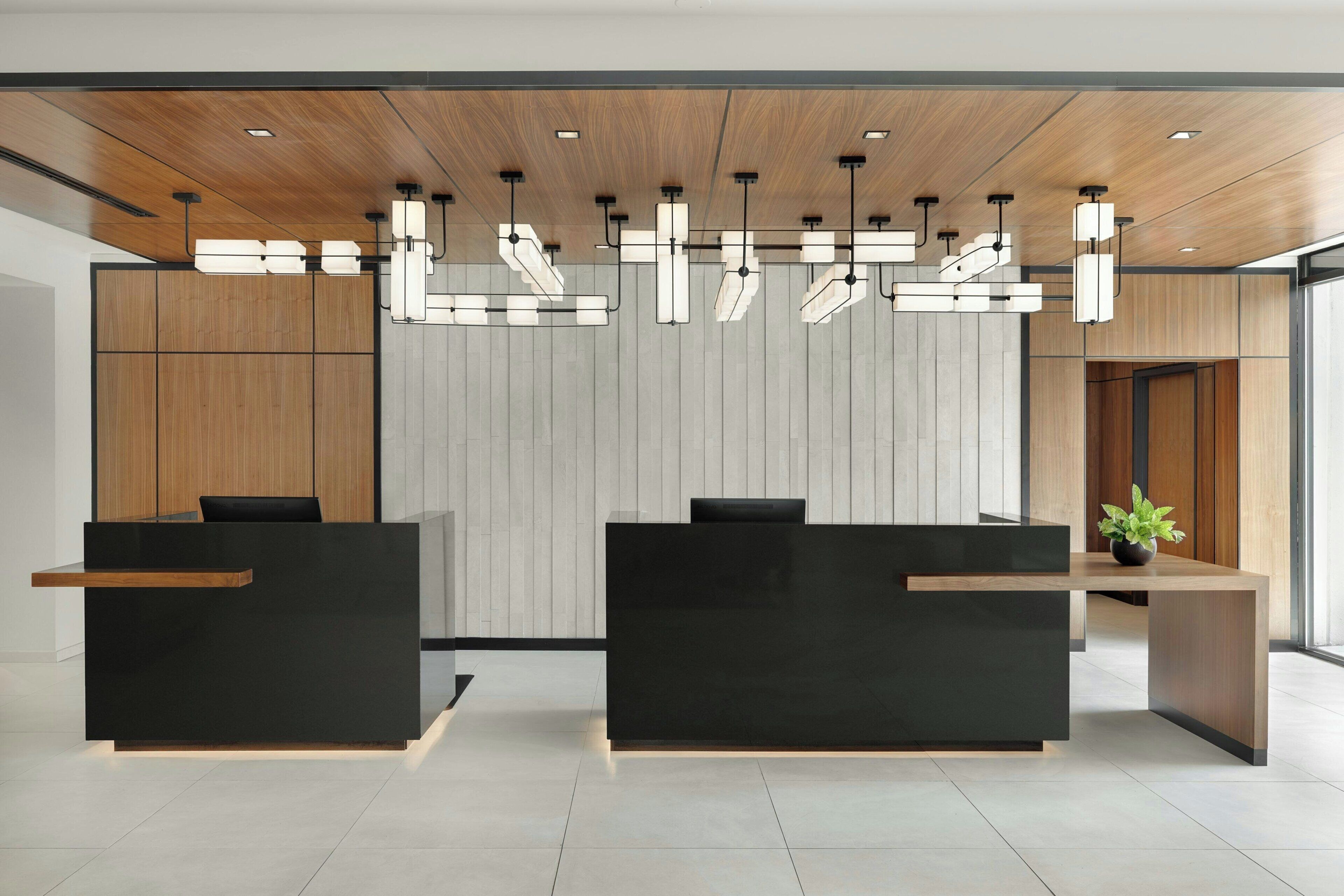 Un moderno mostrador de recepción con dos mostradores negros, paneles de madera en las paredes e iluminación empotrada en el techo.