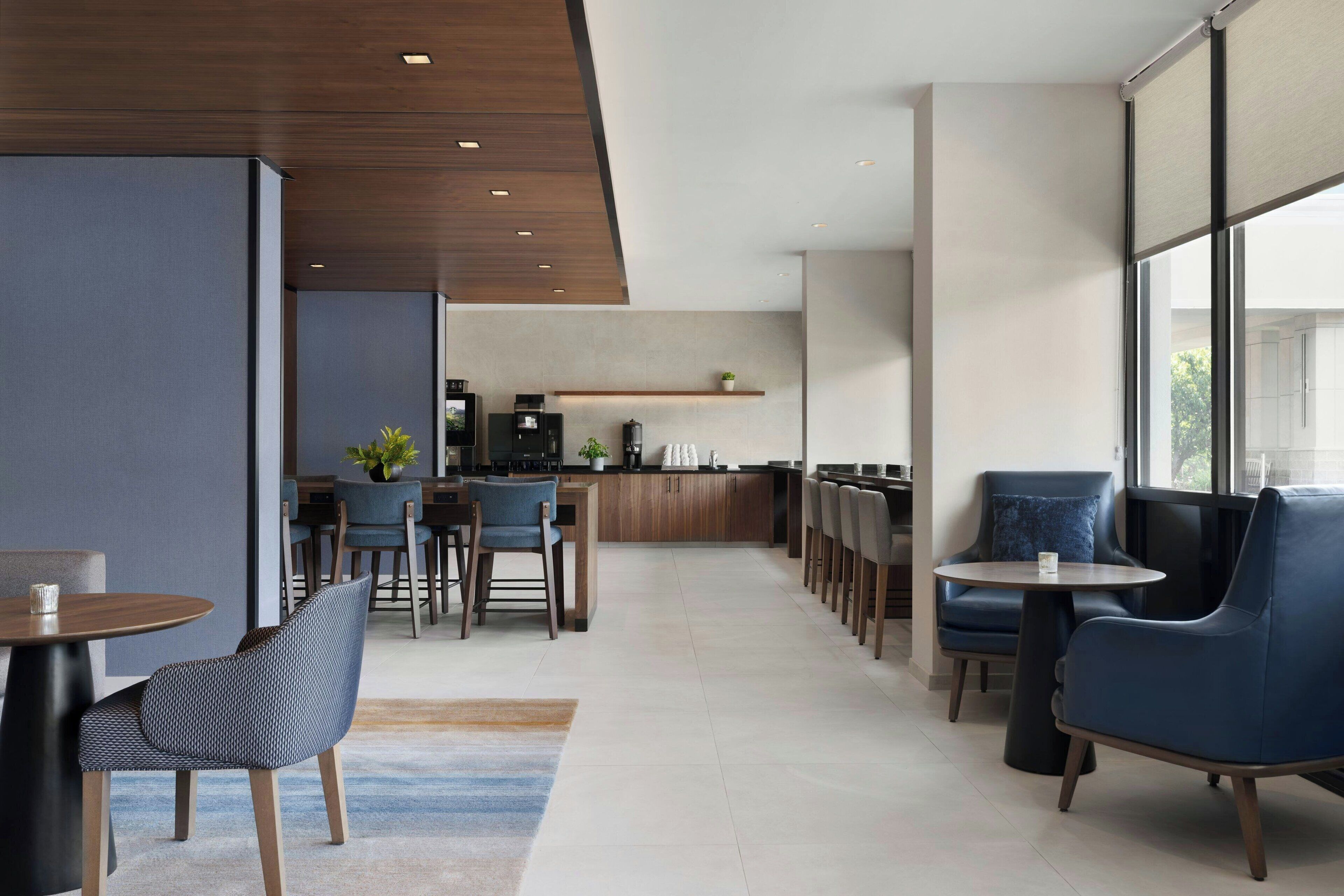 Un hall d'hôtel moderne avec un bar, des espaces pour s'asseoir et une cuisine en arrière-plan.