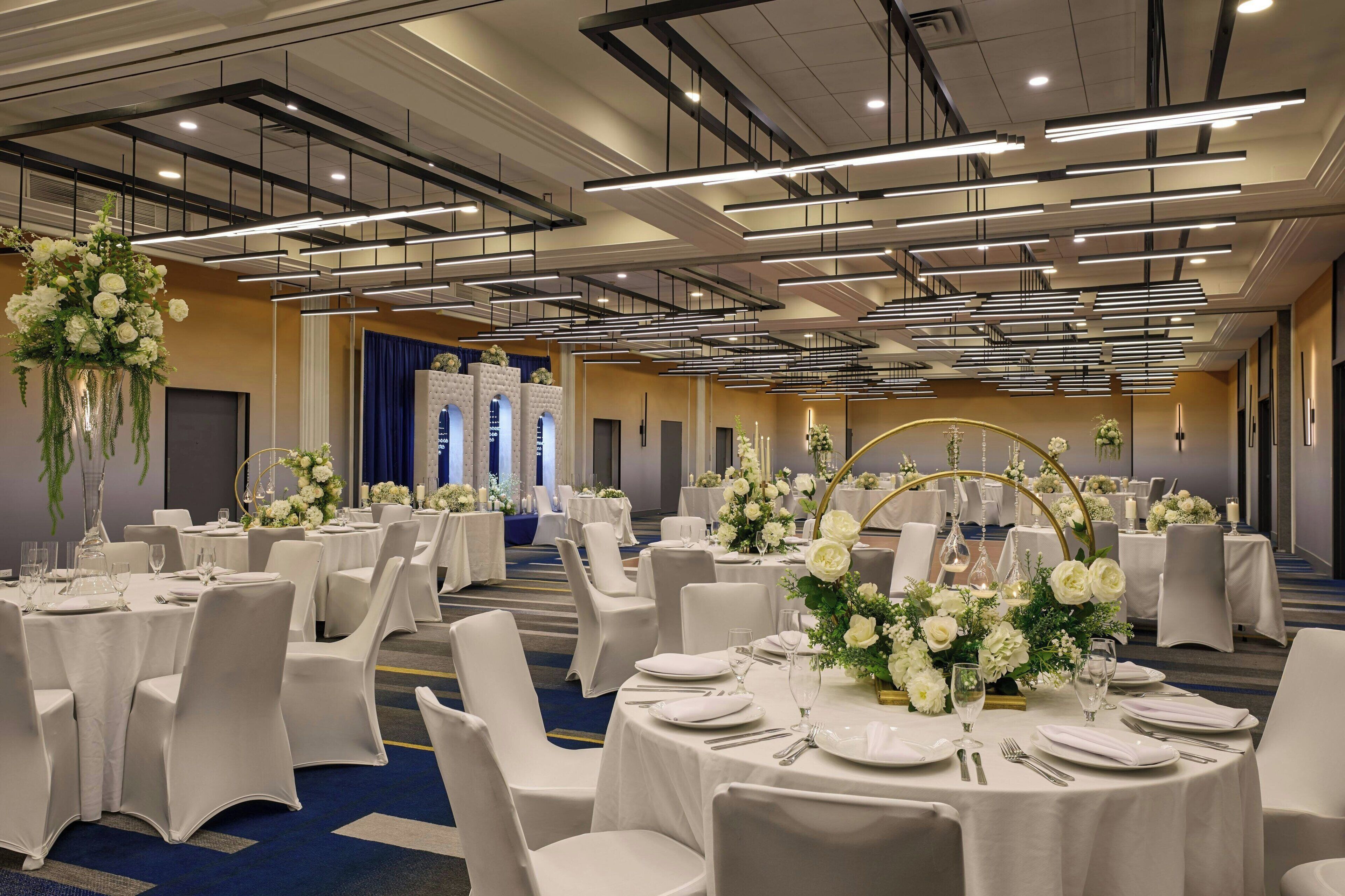 A banquet hall with round tables set for dining, white chairs, and floral centerpieces.