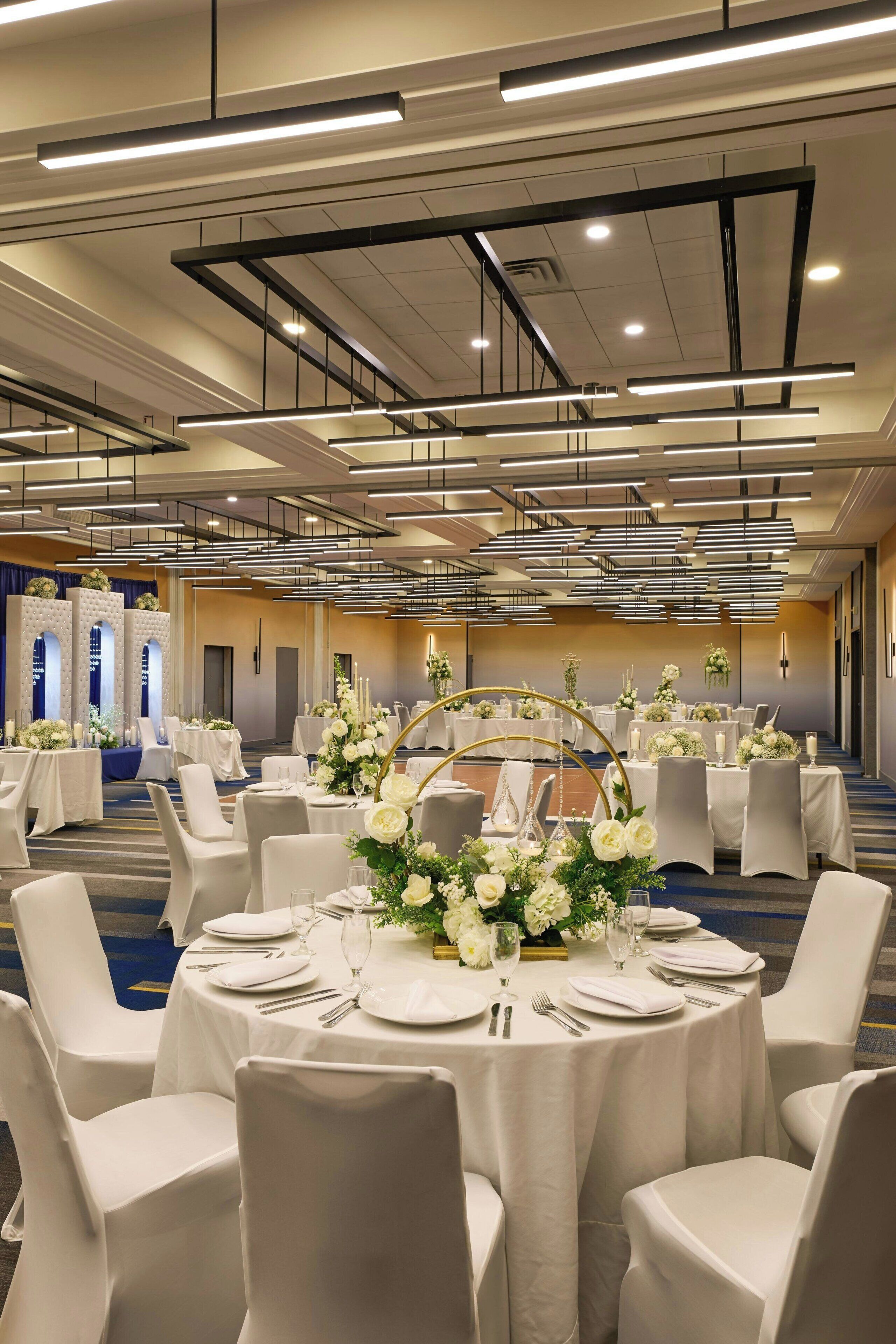 A banquet hall with round tables, white tablecloths, and chairs.