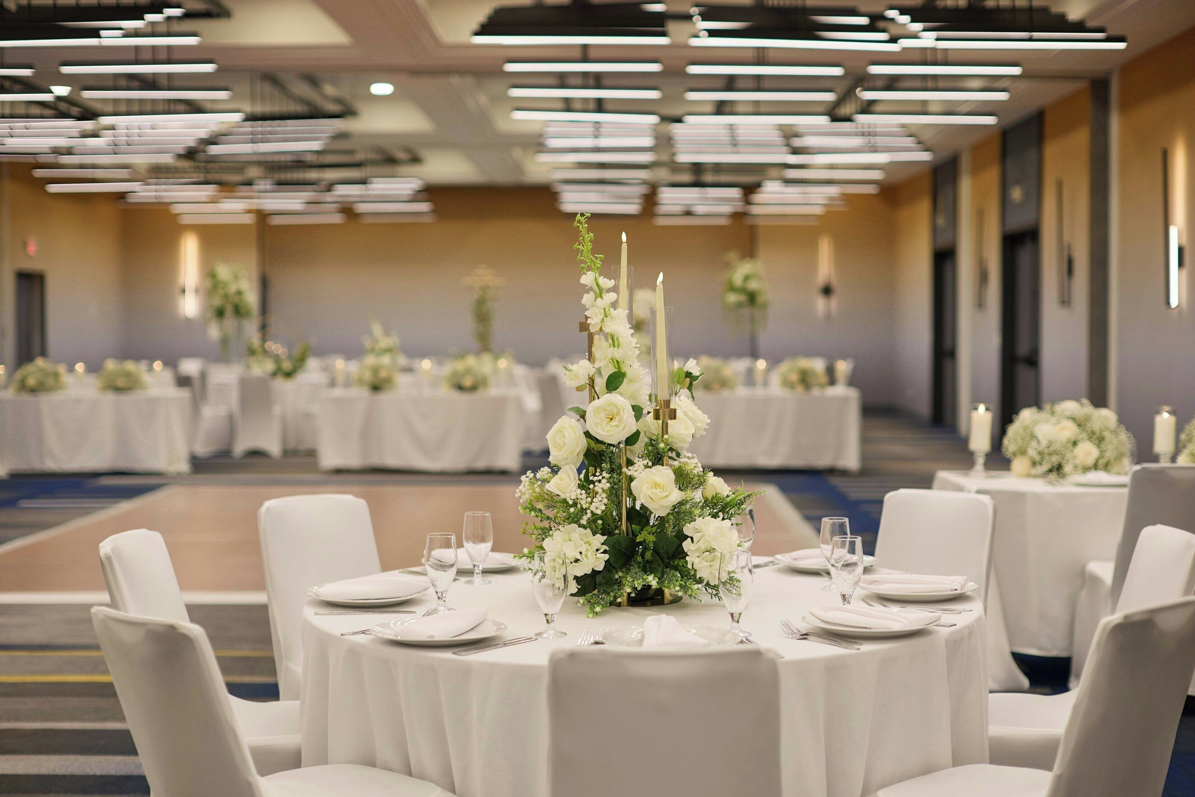 A banquet hall with round tables set for dining, each with white tablecloths, plates, and glasses.