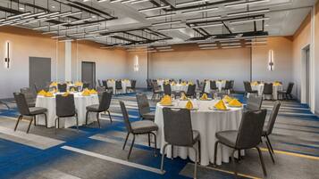 A conference room with multiple round tables, grey chairs, and yellow napkins.