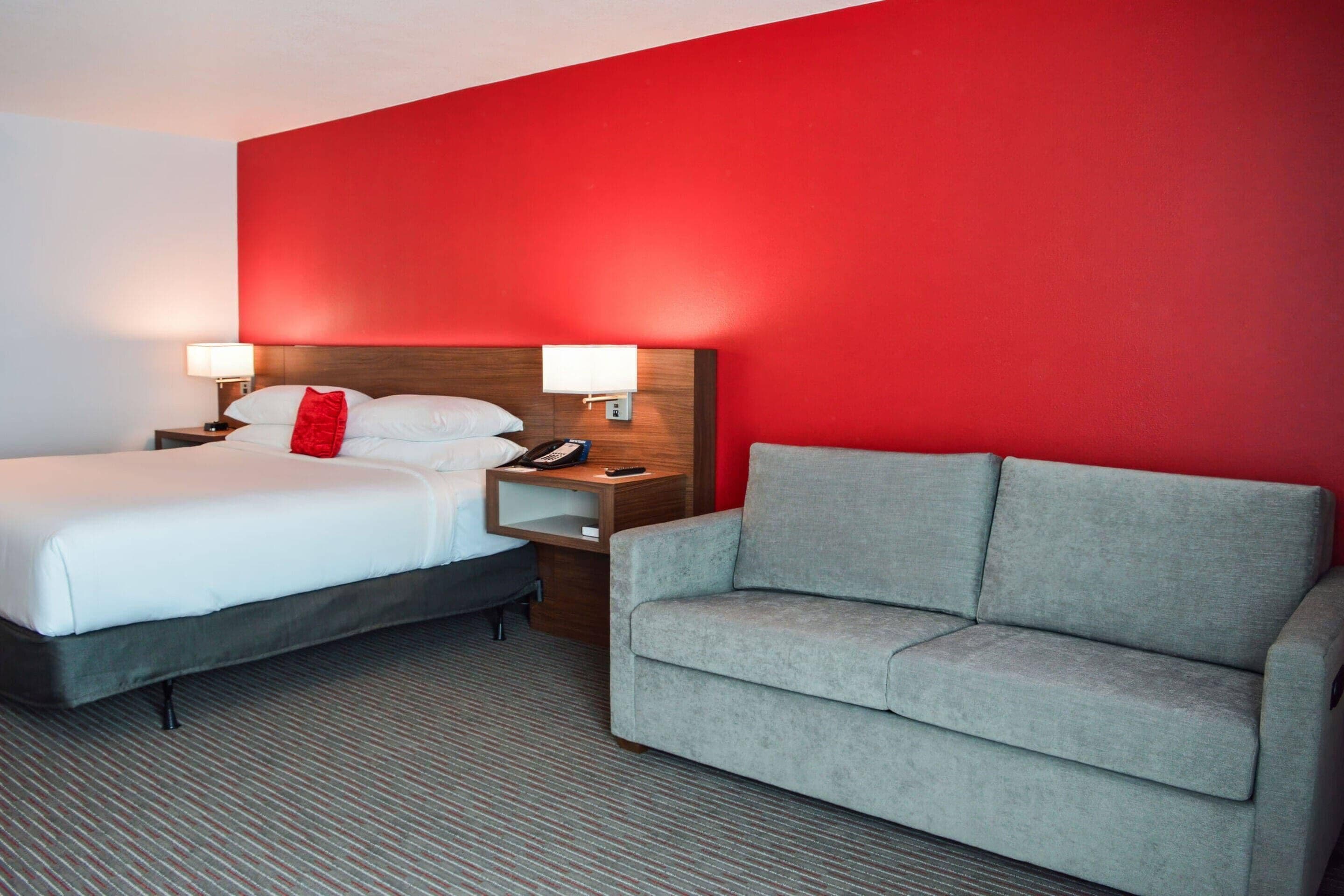 Een hotelkamer met een bed, nachtkastjes, een lamp en een grijze bank.
