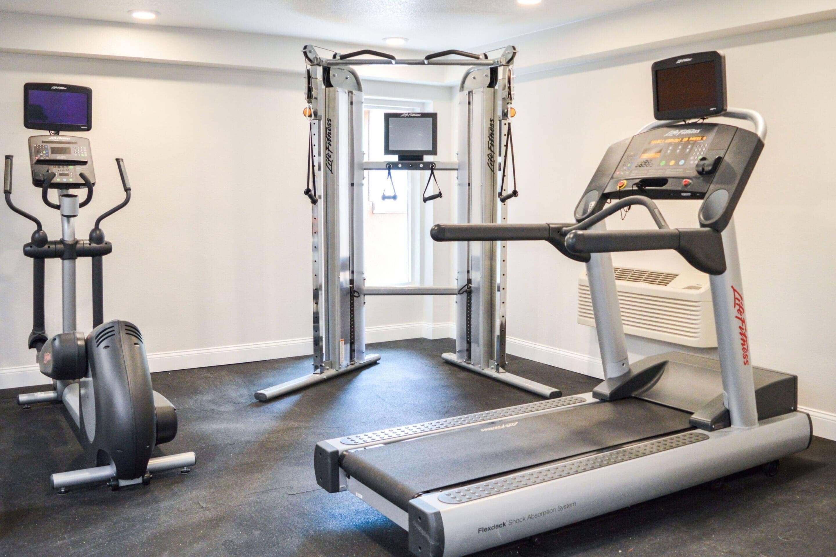Un gimnasio con cinta de correr, máquinas de pesas y barra de dominadas.