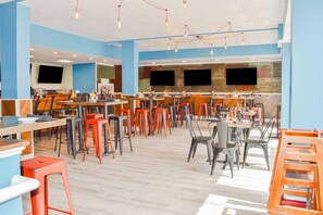 En rymlig restaurang med höga bord och stolar, en bardisk och en stor TV-skärm.