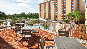 A hotel rooftop with a swimming pool, outdoor seating, and a view of the surrounding greenery.