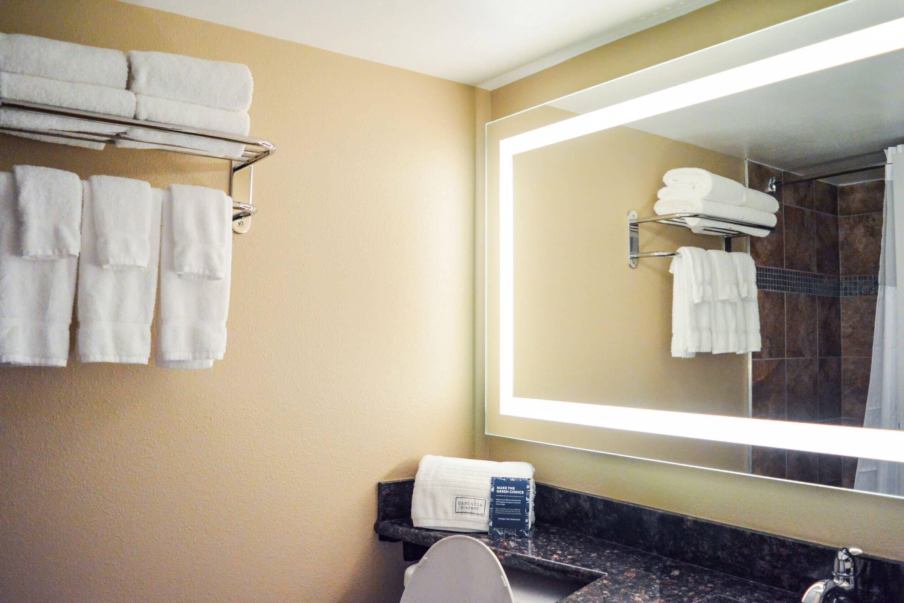 A bathroom with a large mirror, multiple white towels on a rack, a sink, and a shower area.