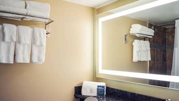 A bathroom with a large mirror, multiple white towels on a rack, a sink, and a shower area.