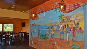 A restaurant with a mural of a beach scene, wooden tables and chairs, and a bar area with bottles. - Radisson Hotel Orlando Lake Buena Vista South (Kissimmee)