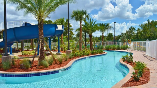 A swimming pool with a blue slide, surrounded by palm trees and a fenced area. - Radisson Hotel Orlando Lake Buena Vista South (Kissimmee)