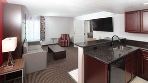 A modern hotel room with a kitchenette, a sofa, a coffee table, a TV mounted on the wall, and a patterned rug. - Radisson Hotel Orlando Lake Buena Vista South (Kissimmee)