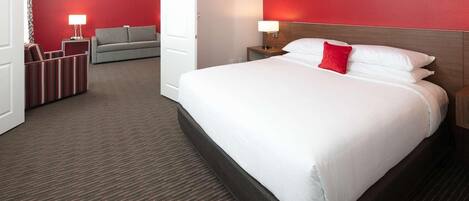 A hotel room with a large bed, a sofa, a nightstand, and a red accent wall.