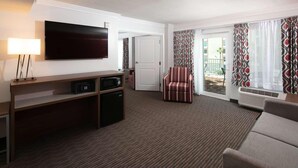 A hotel room with a flat-screen TV, a desk with a lamp, a chair, a sofa, and a sliding glass door leading to a balcony. - Radisson Hotel Orlando Lake Buena Vista South (Kissimmee)