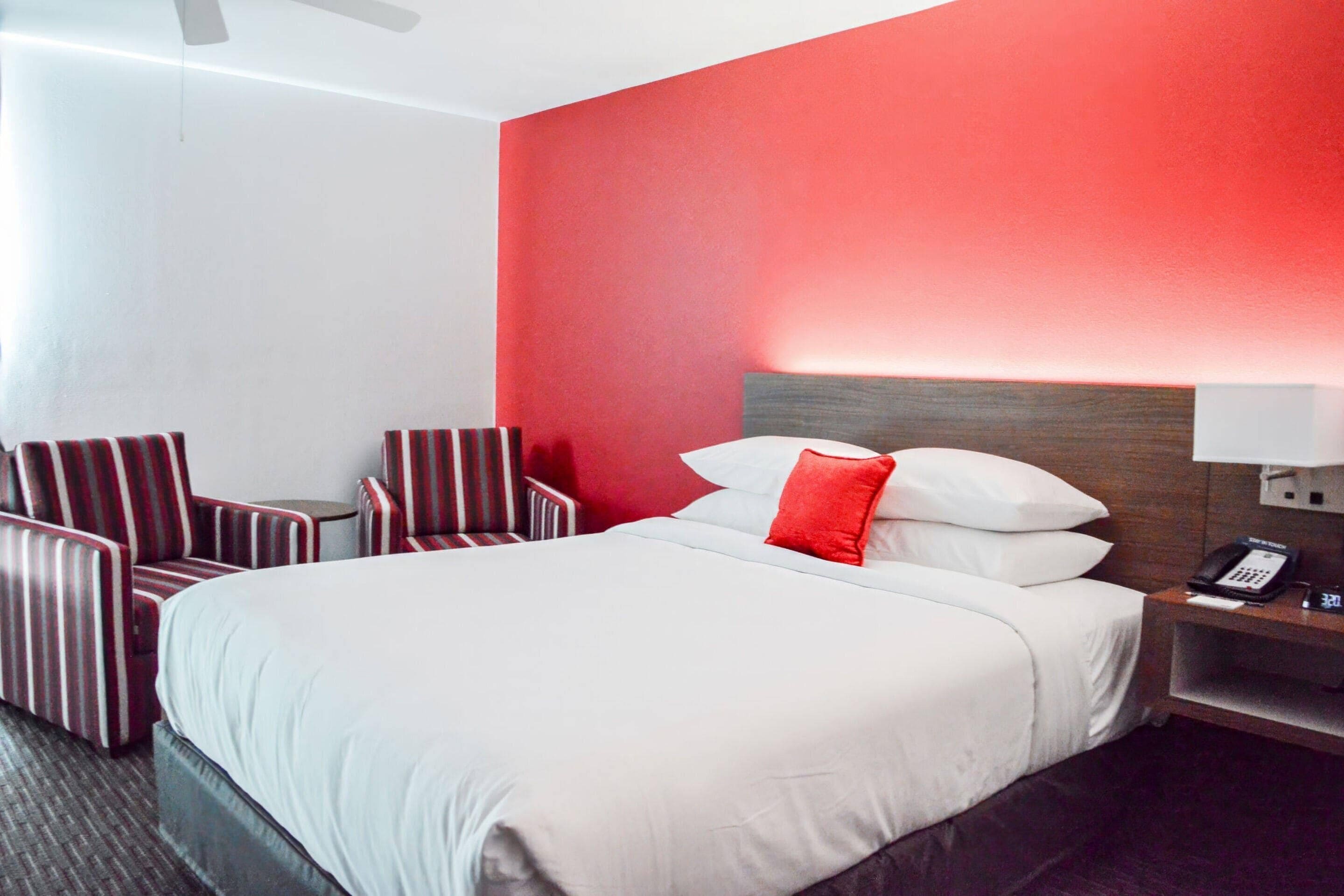 Una camera d'albergo con un letto grande, un comodino con il telefono e due poltrone a righe.