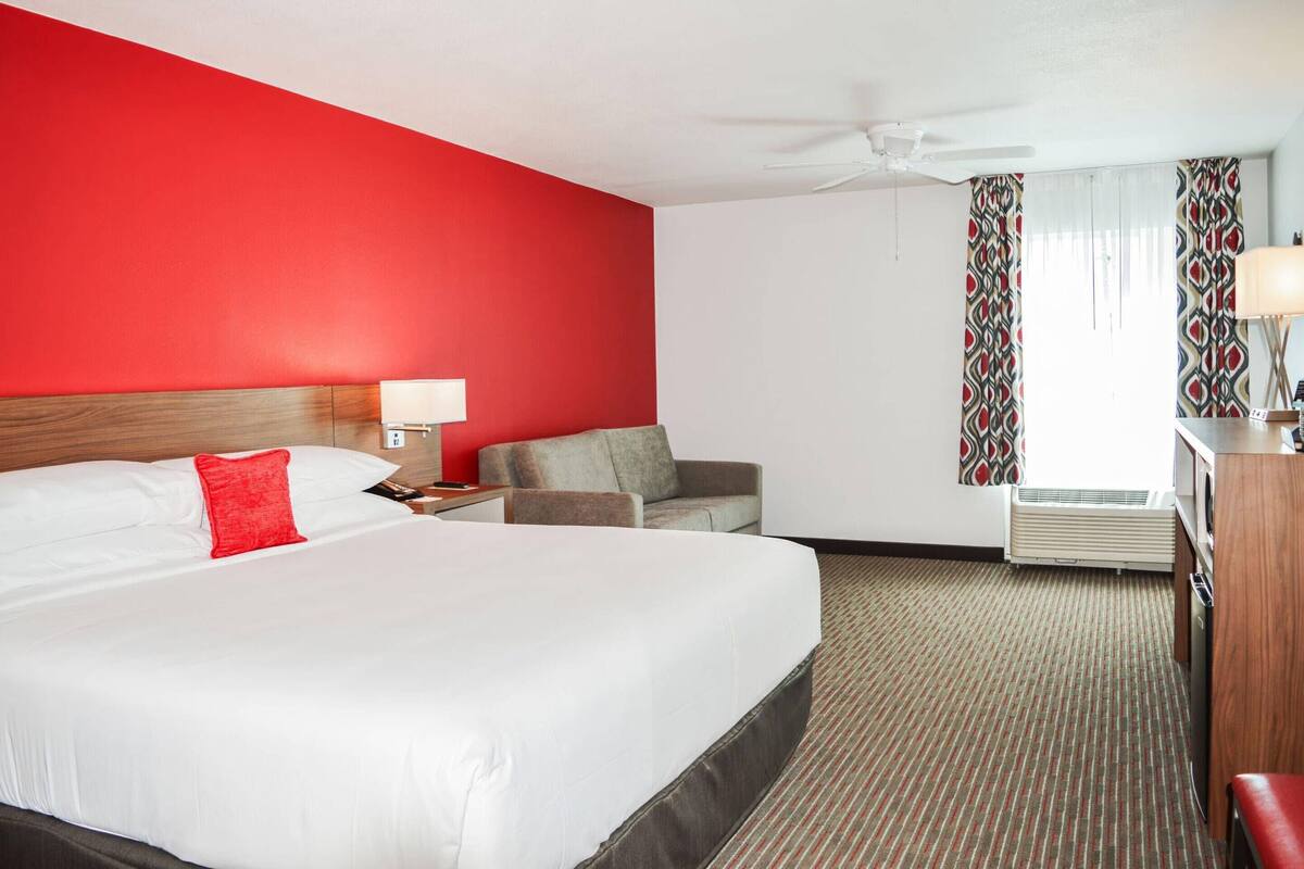 Ein Hotelzimmer mit einem großen Bett, einem Schreibtisch mit Lampe, einem Sessel und einer Klimaanlage.
