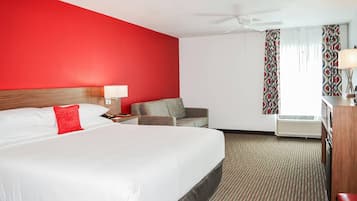 A hotel room with a large bed, a desk with a lamp, a chair, and an air conditioning unit.