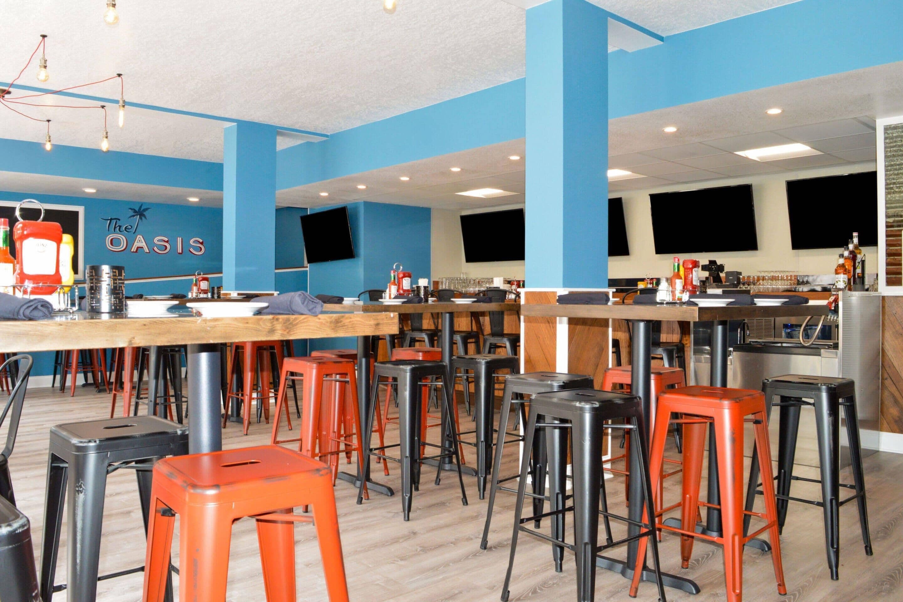 A restaurant with blue walls, multiple tables and stools, and a sign reading "The Oasis".