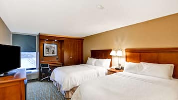 A hotel room with two beds, a desk with a flat-screen TV, a chair, and a window with a view.